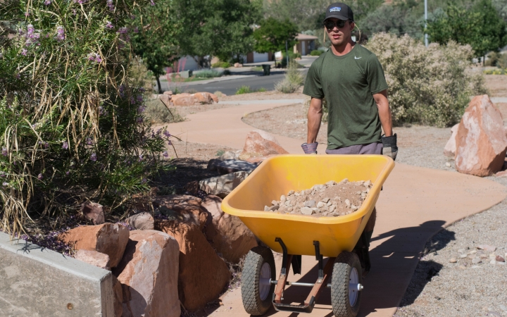 A person pushes a wheelbarrow full of rocks during a service project with outward bound.